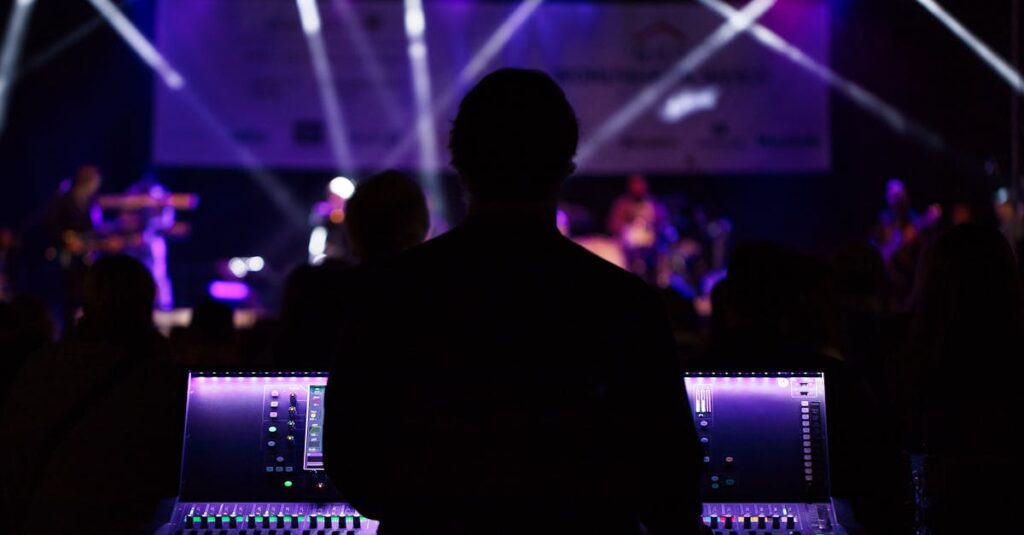 A sound engineer manages the audio mixer during a vibrant live concert with colorful lighting.