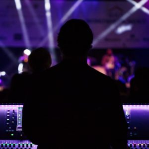 A sound engineer manages the audio mixer during a vibrant live concert with colorful lighting.